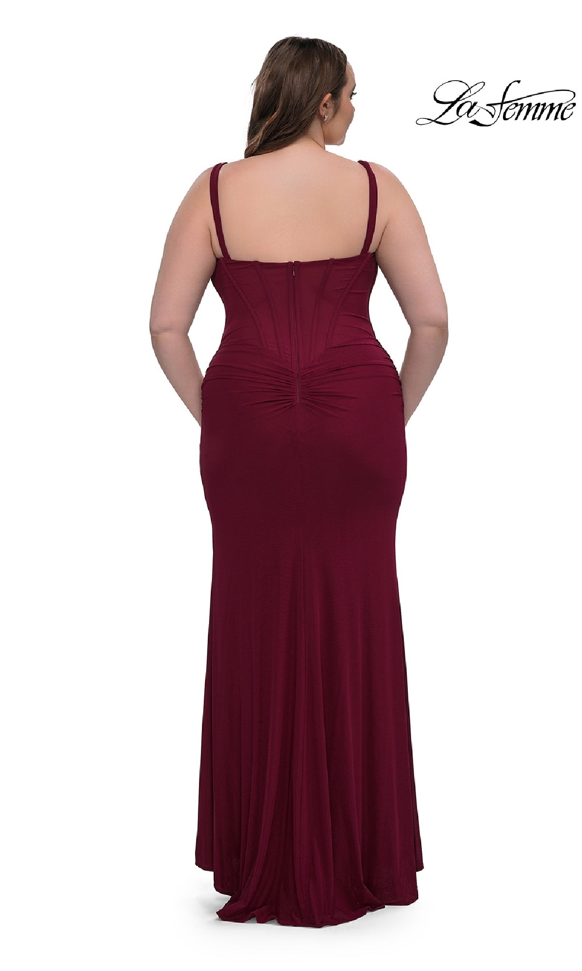 A woman wears the La Femme 33015, a plus-size long corset prom dress in burgundy with ruched back detail. The sleeveless, floor-length fitted formal dress is shown from behind against a white background.